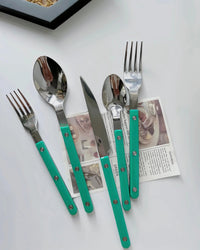 Close-up of turquoise modern French rivet cutlery with sleek handles on a kitchen table.