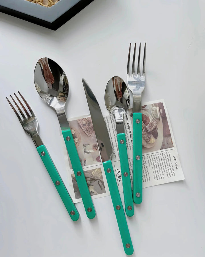 Close-up of turquoise modern French rivet cutlery with sleek handles on a kitchen table.