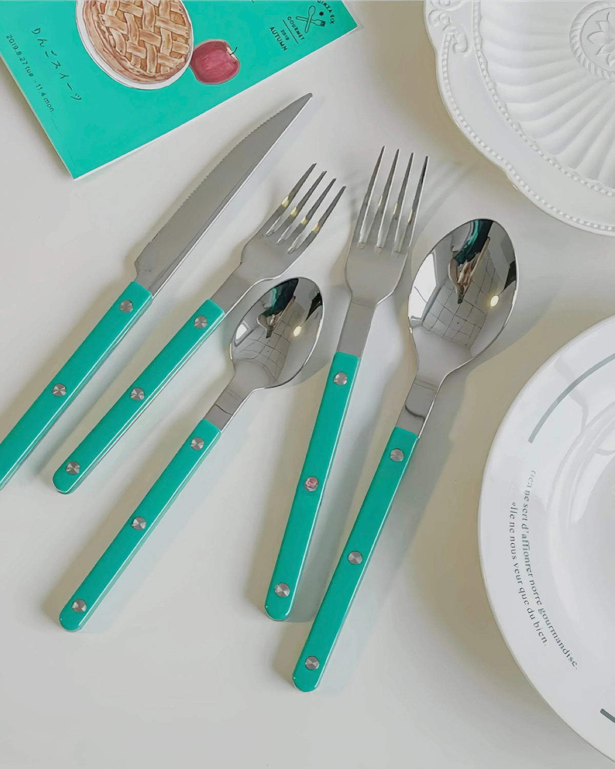 Turquoise bistrot style flatware set arranged neatly on a gray textured surface.