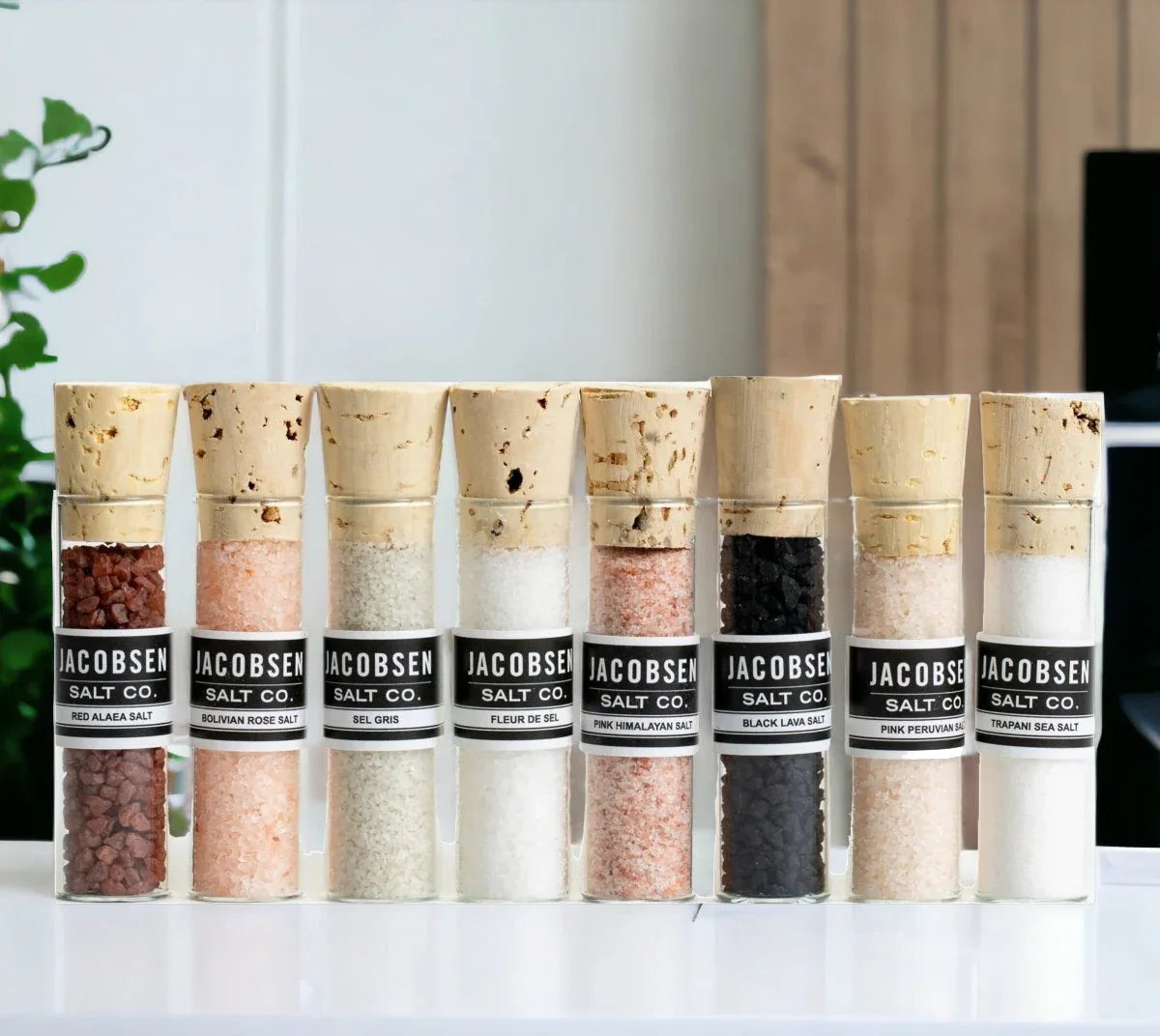 Close-up of various gourmet salts spilling from small glass vials on a white surface.