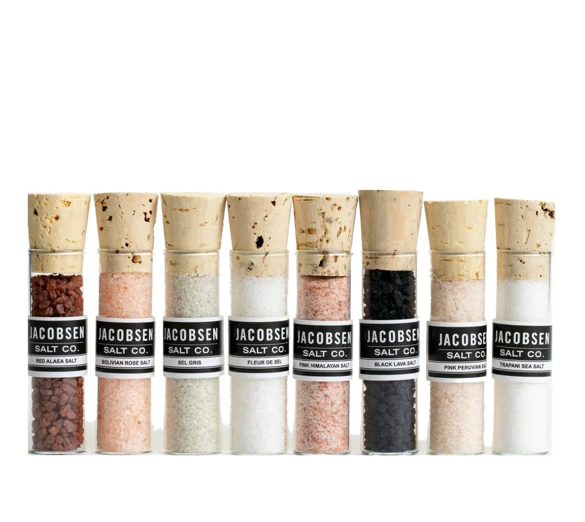Eight clear glass vials of sourced salt arranged in a gift box with colorful salt flakes inside.