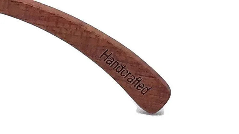 Hand holding Brazilian pear wood sunglasses with vibrant ice blue polarized lenses outdoors.
