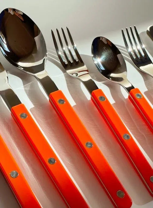French bistrot style dopamine flatware set stacked and spread on a dark textured background.