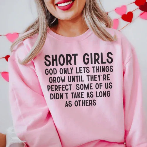 Light pink sweatshirt featuring white text 'Short Girls God Only Lets Things Grow Until They're Perfect'