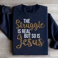 Close-up of black sweatshirt showing the text 'The Struggle Is Real But So Is Jesus' in white lettering.