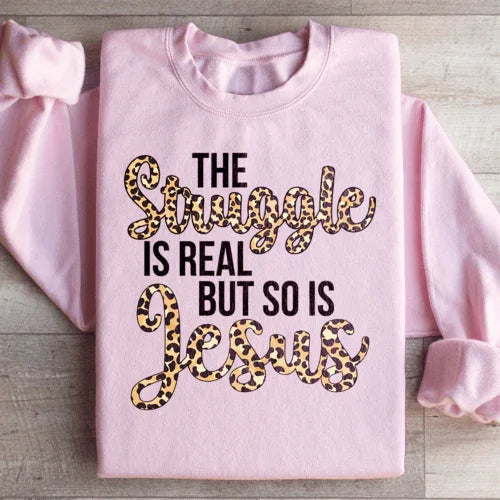 Light pink sweatshirt with large white text saying 'The Struggle Is Real But So Is Jesus'.
