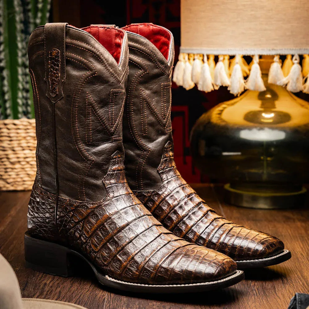 Lifestyle image of man wearing Tucson aged brown caiman belly skin cowboy boots outdoors.