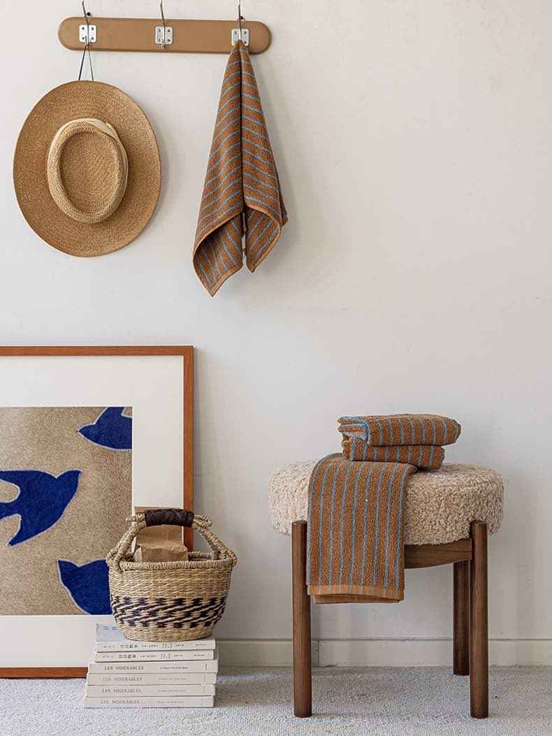 Vintage style striped bath towel hanging on a silver hook against a white tiled bathroom wall.