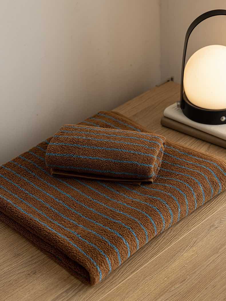 Rolled retro stripe bath towel showing soft organic cotton texture and warm earthy colors.