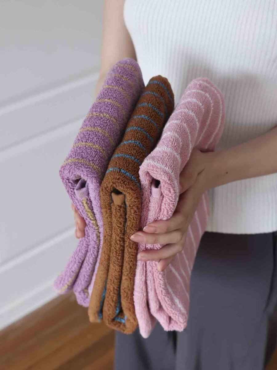 Folded retro stripe bath towel in warm colors on a white surface, showing soft texture of organic cotton.