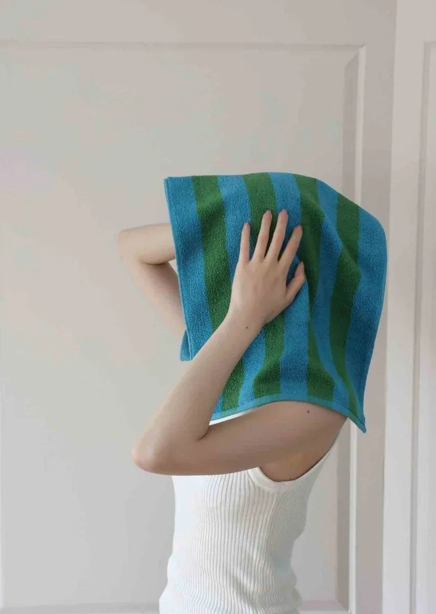 Colorful striped bath towel folded neatly on wooden surface with sunlight.