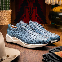 Model walking outdoors wearing navy blue ostrich skin sneakers paired with casual pants.