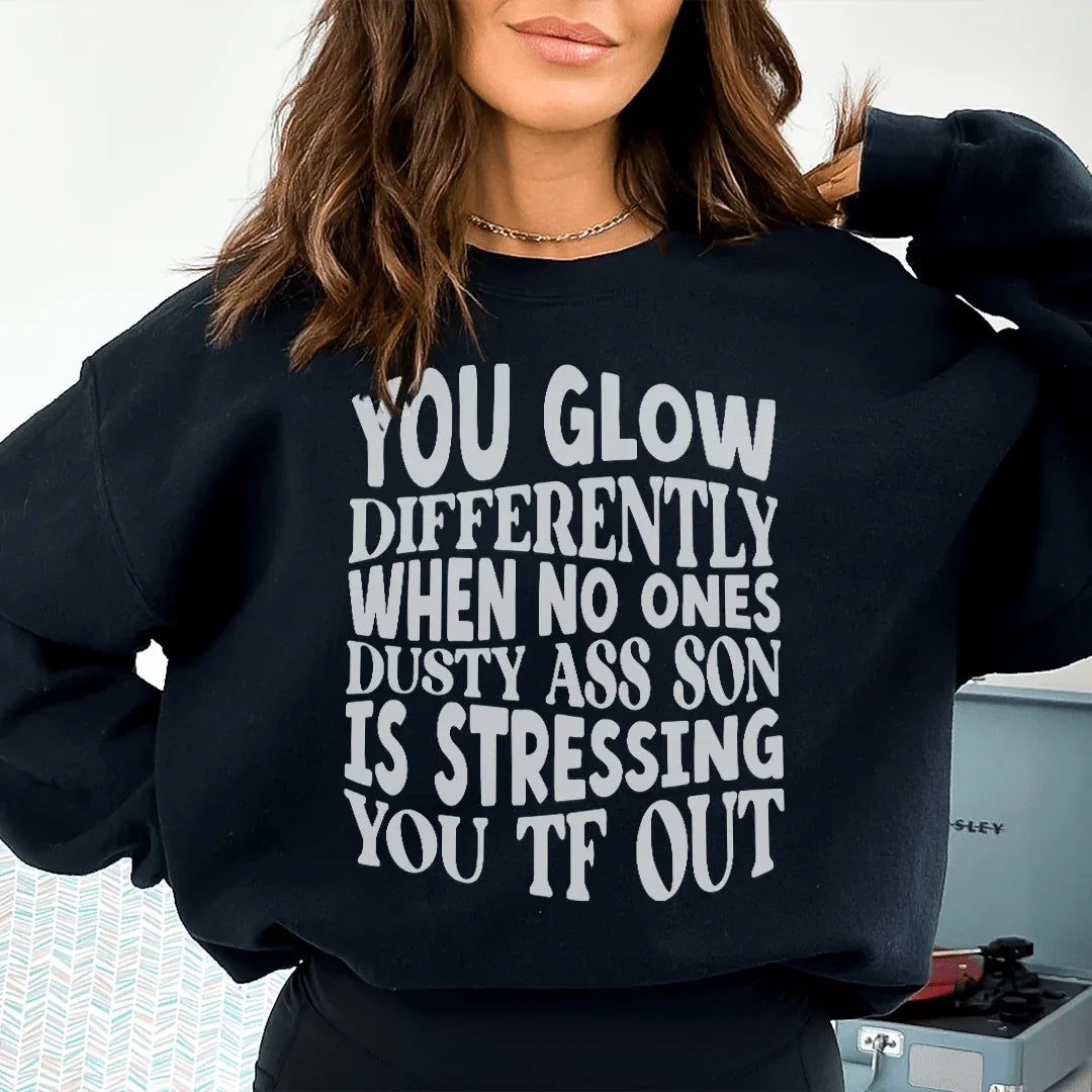 Black sweatshirt with text 'You Glow Differently When No Ones Dusty A-s Son Is' in peachy font.