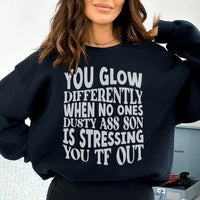 Black sweatshirt with text 'You Glow Differently When No Ones Dusty A-s Son Is' in peachy font.