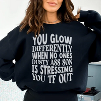 Close-up of black sweatshirt with peach-colored text 'You Glow Differently When No Ones Dusty A-s Son Is'.