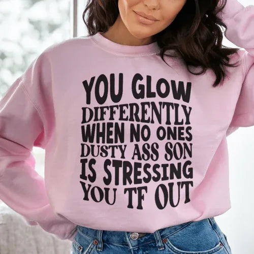Light pink sweatshirt with peachy text saying 'You Glow Differently When No Ones Dusty A-s Son Is'.