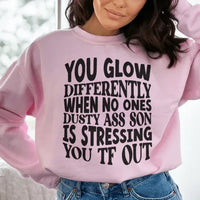 Light pink sweatshirt with peachy text saying 'You Glow Differently When No Ones Dusty A-s Son Is'.