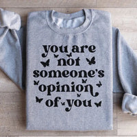 Close-up of sweatshirt's front text saying 'You're Not Someone's Opinion Of You' with peach fabric background.