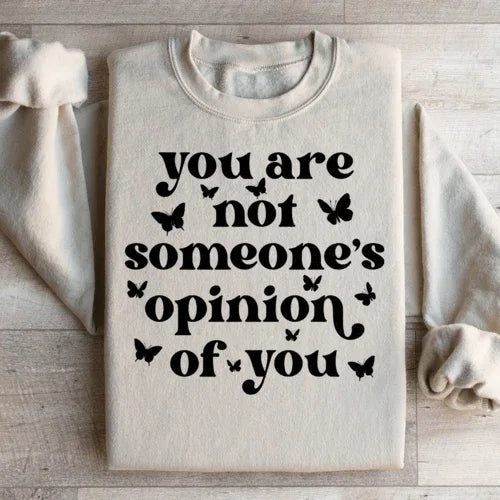 Sweatshirt laid flat showing full front text 'You're Not Someone's Opinion Of You' on peach fabric.